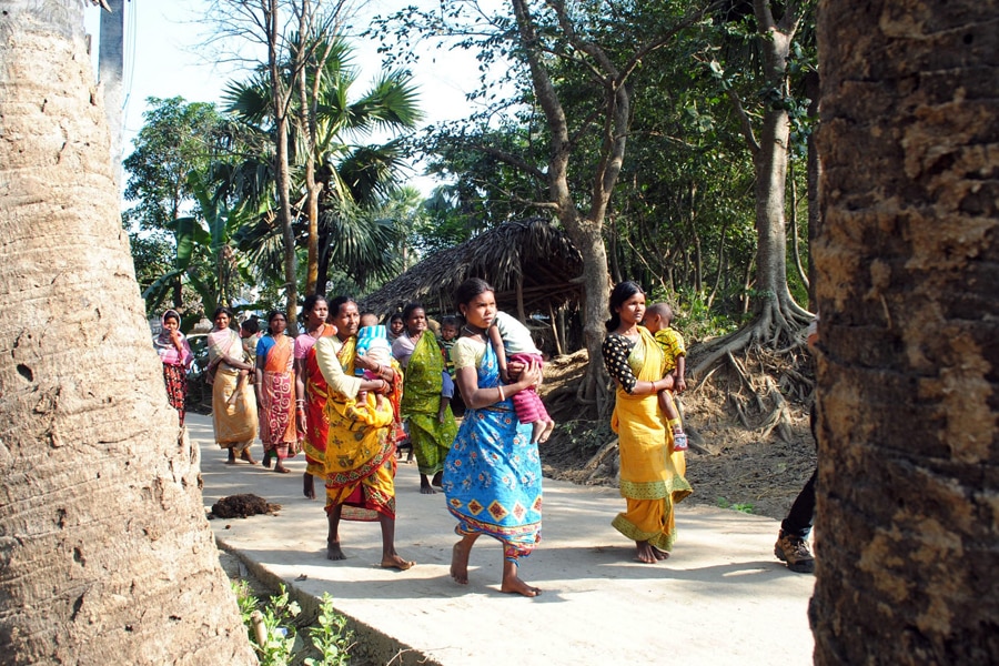 Santhal tribal women carry children and walk in a village where a woman was gang raped