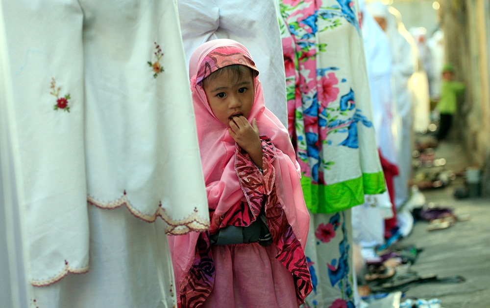 A Muslim girl stands with women offering prayers to mark the Eid al-Adha holiday on a street in Bali, Indonesia